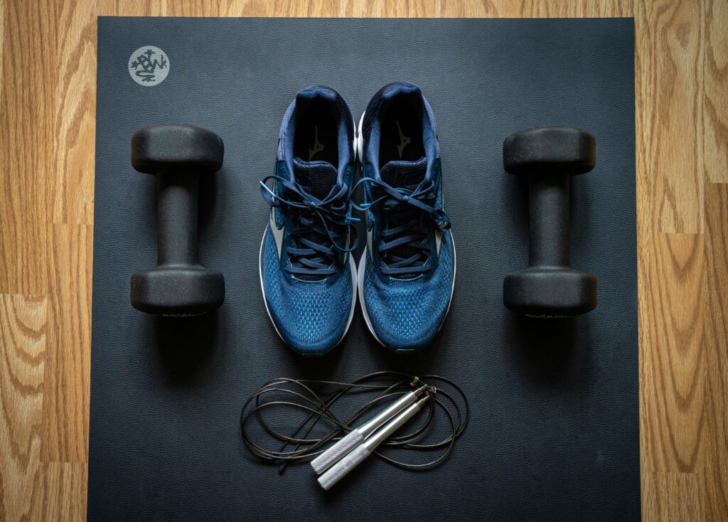 Pair of shoes on a yoga mat, skipping rope and two dumbbells