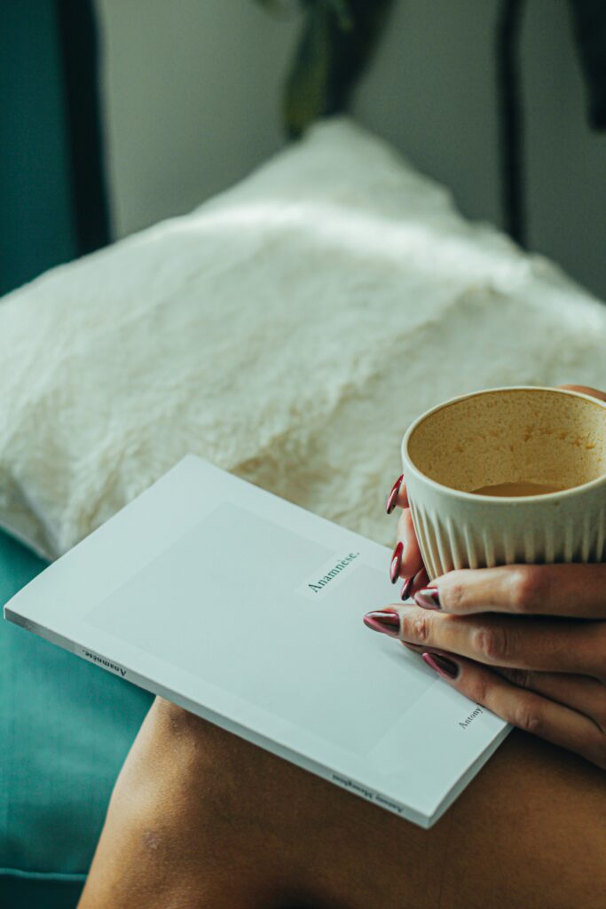 Female hands holding a book on her lap and a cup of coffee