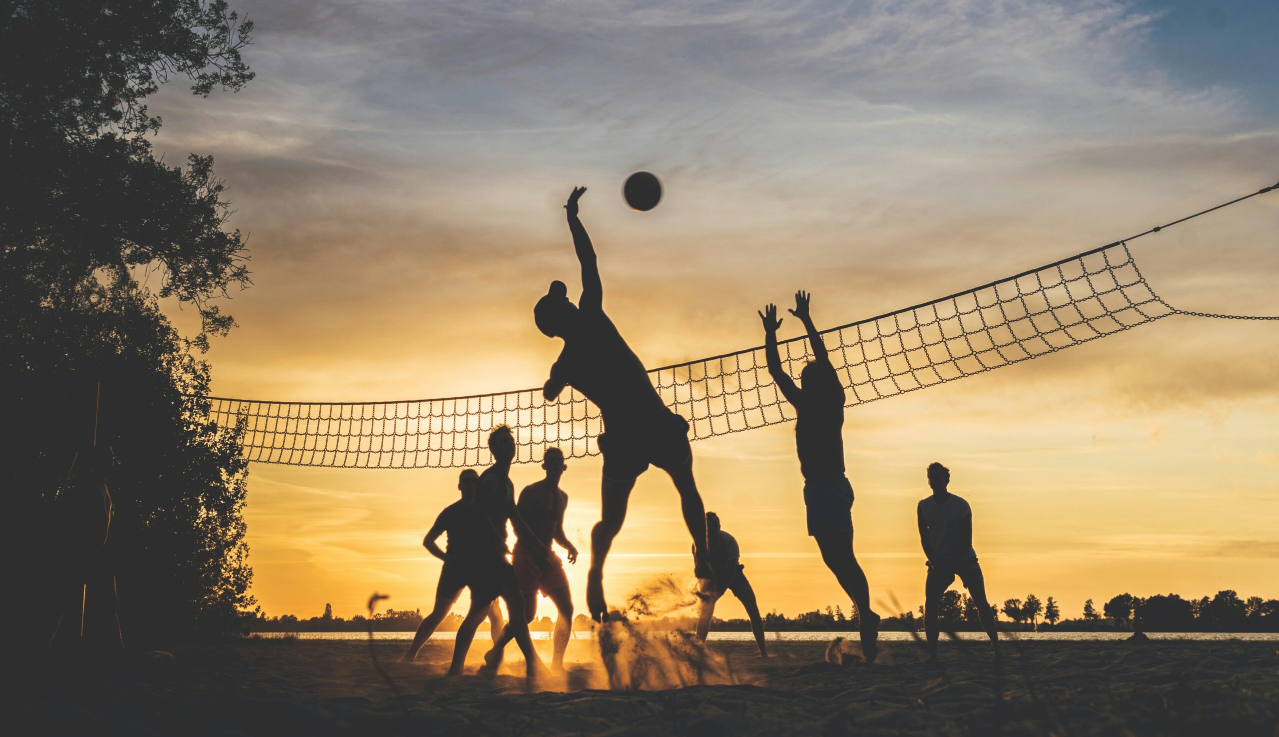 A group of people playing volleyball at sunset