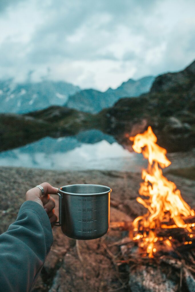 A hand holds a metal cup in front of the campfire