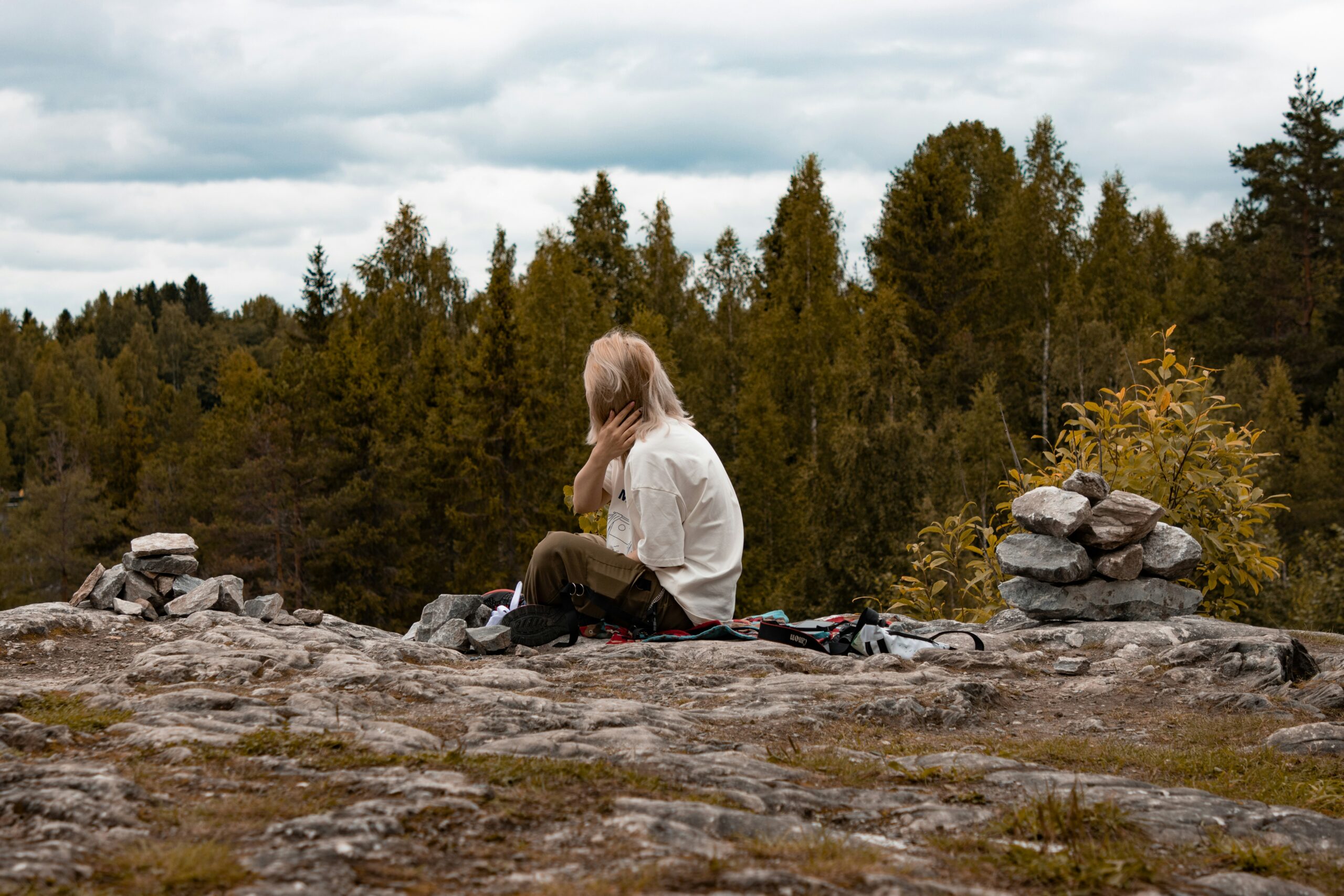 A woman sits with her back to the camera on a rock in the mountains
