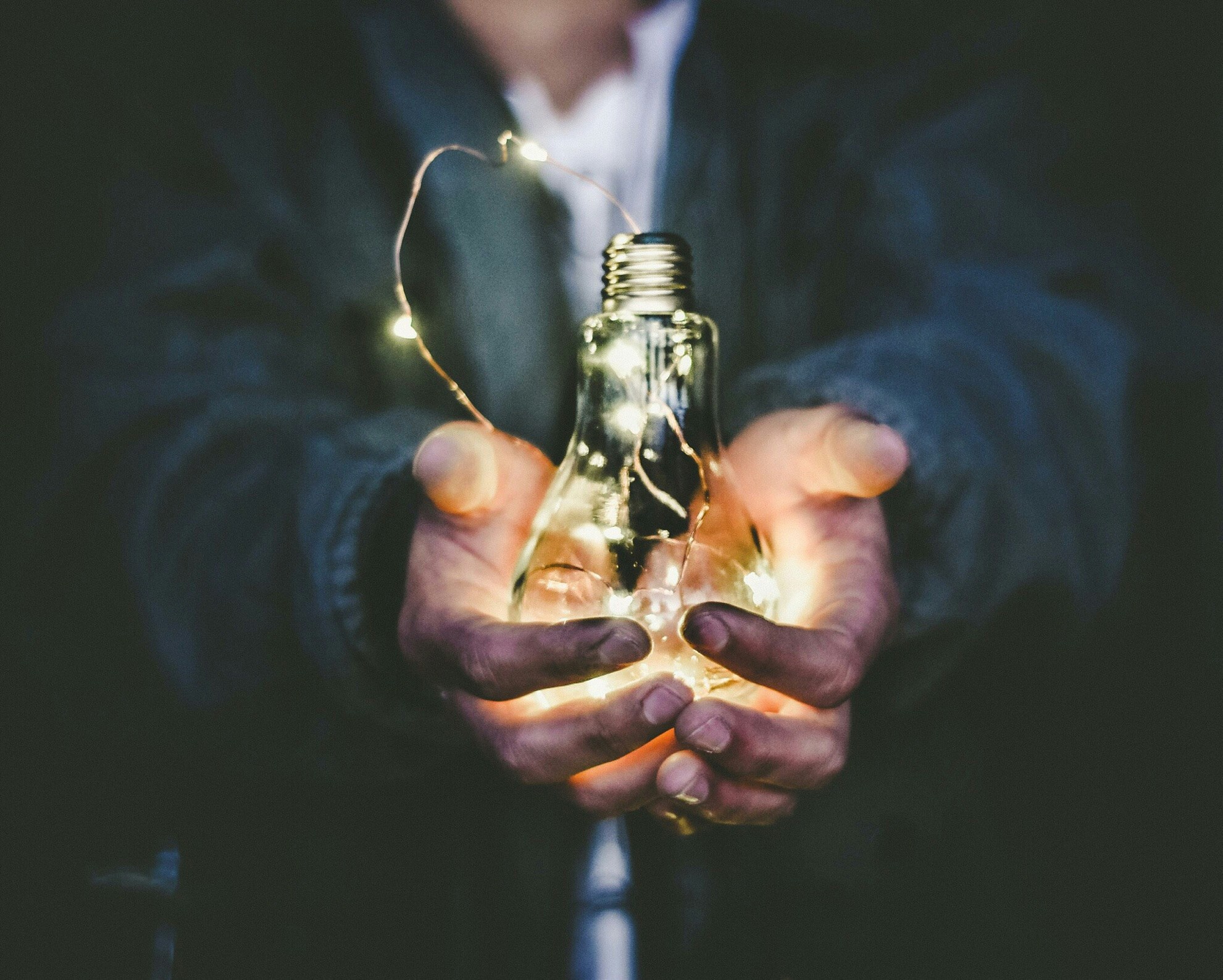 Two hands holding a light bulb with a string of lights inside